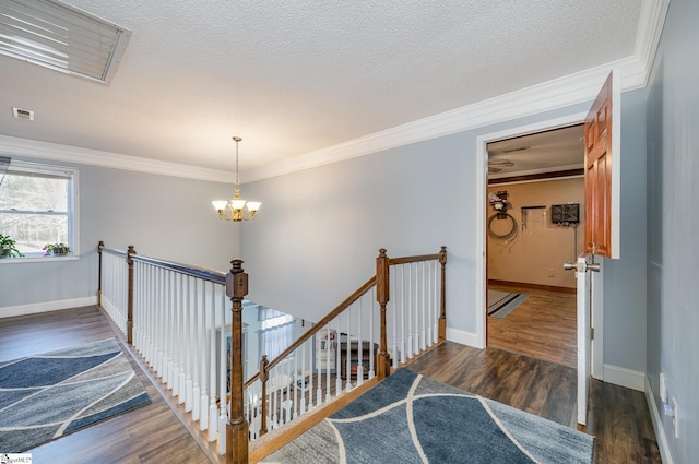 staircase featuring an inviting chandelier, ornamental molding, a textured ceiling, and hardwood / wood-style floors