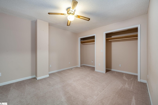 unfurnished bedroom with two closets, a textured ceiling, light colored carpet, and ceiling fan