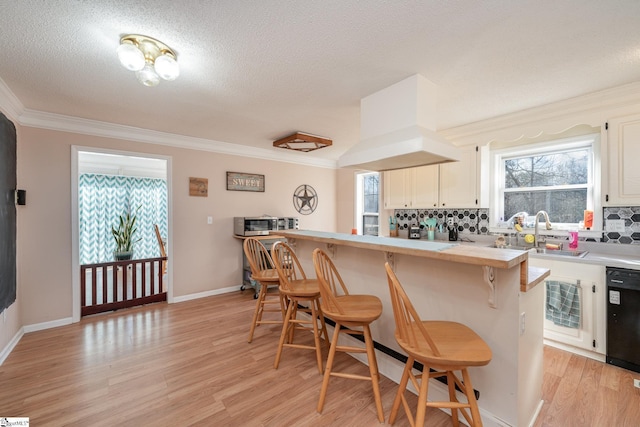 kitchen with dishwasher, light hardwood / wood-style floors, a breakfast bar, sink, and backsplash