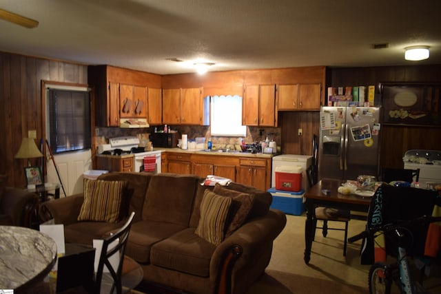 kitchen featuring a textured ceiling, white stove, wood walls, and stainless steel refrigerator with ice dispenser