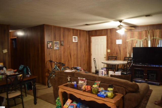 living room with light colored carpet, ceiling fan, wooden walls, and a textured ceiling