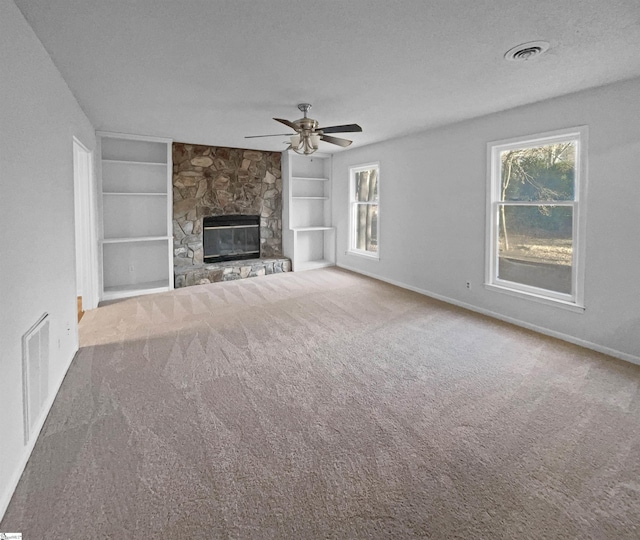 unfurnished living room with a textured ceiling, a stone fireplace, built in features, and carpet flooring