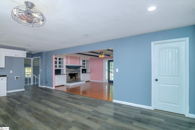 unfurnished living room with a textured ceiling, dark hardwood / wood-style flooring, and a stone fireplace