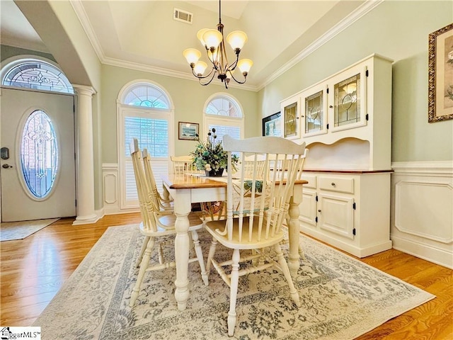 dining space with ornate columns, a chandelier, a healthy amount of sunlight, and light hardwood / wood-style flooring