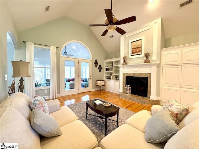 living room featuring a fireplace, light wood-type flooring, high vaulted ceiling, and ceiling fan