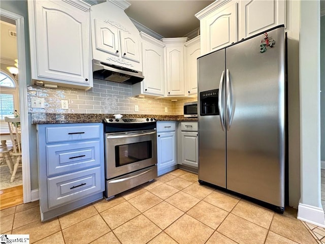 kitchen with stainless steel appliances, dark stone counters, light tile patterned floors, and white cabinetry