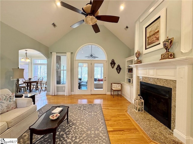 living room with light hardwood / wood-style flooring, a premium fireplace, french doors, high vaulted ceiling, and ceiling fan