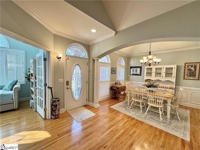 foyer featuring vaulted ceiling, light hardwood / wood-style floors, ornate columns, an inviting chandelier, and crown molding