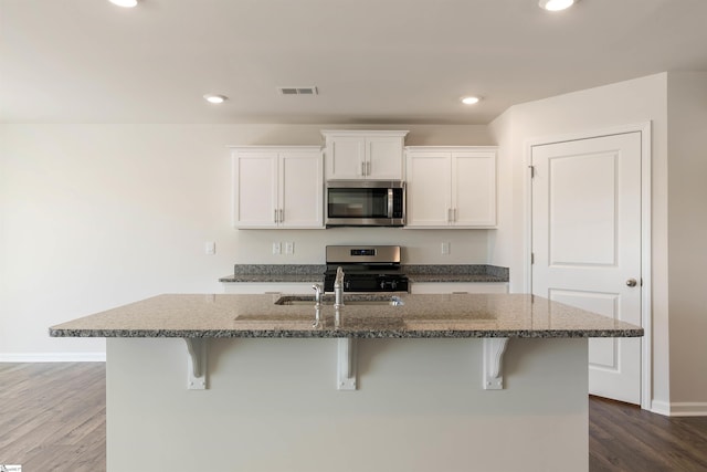 kitchen with dark wood-type flooring, a center island with sink, appliances with stainless steel finishes, and white cabinetry