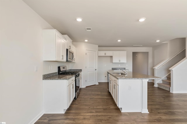 kitchen featuring appliances with stainless steel finishes, an island with sink, white cabinetry, and light stone countertops