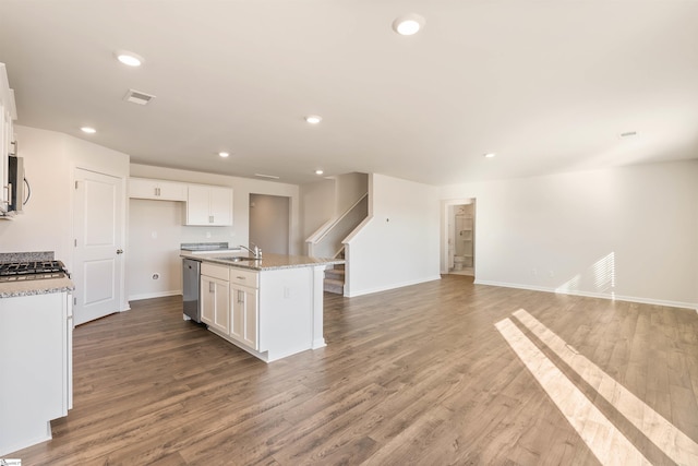 kitchen with light stone countertops, stainless steel dishwasher, a kitchen island with sink, white cabinets, and wood-type flooring