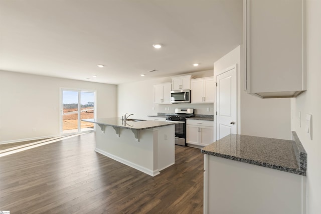 kitchen with appliances with stainless steel finishes, dark stone counters, dark wood-type flooring, white cabinets, and sink