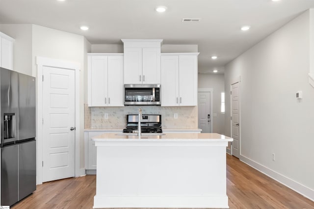 kitchen with stainless steel appliances, white cabinets, light wood-type flooring, an island with sink, and decorative backsplash