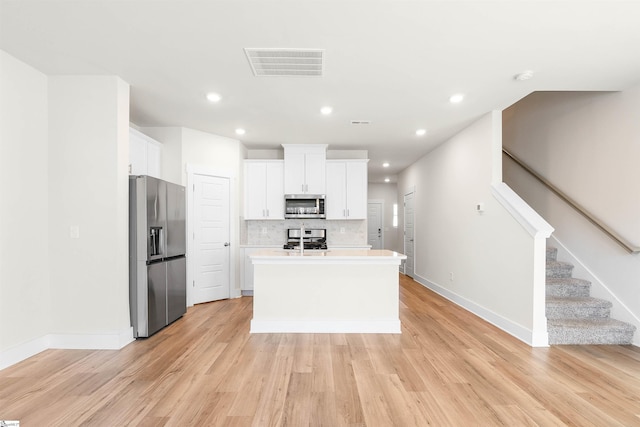 kitchen with light hardwood / wood-style flooring, stainless steel appliances, a center island with sink, backsplash, and white cabinetry