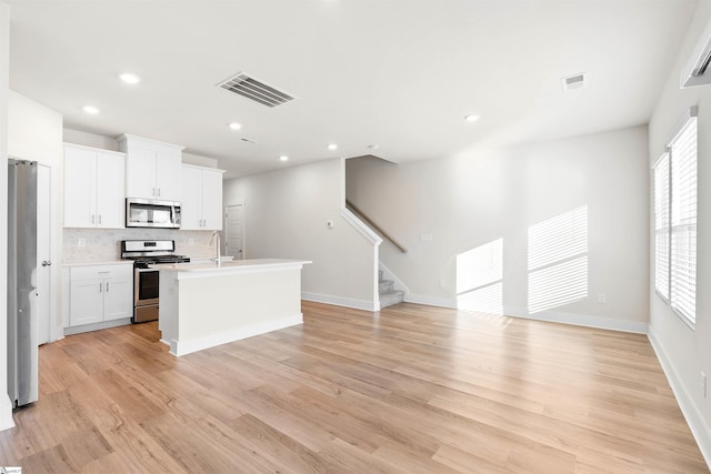 kitchen with stainless steel appliances, an island with sink, a healthy amount of sunlight, white cabinetry, and tasteful backsplash