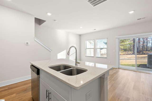 kitchen featuring light stone counters, dishwasher, light hardwood / wood-style flooring, a center island with sink, and sink