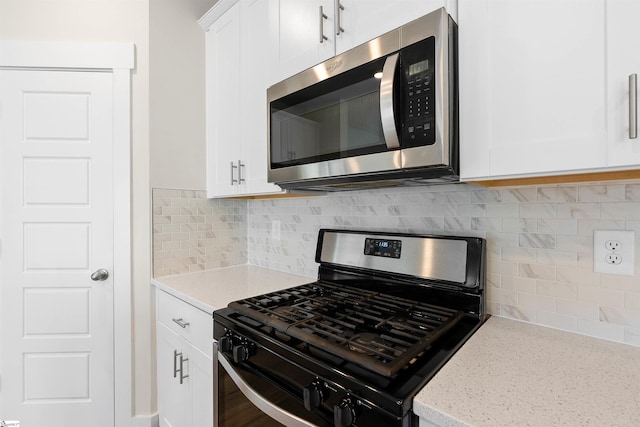 kitchen featuring white cabinetry, backsplash, range with gas stovetop, and light stone countertops