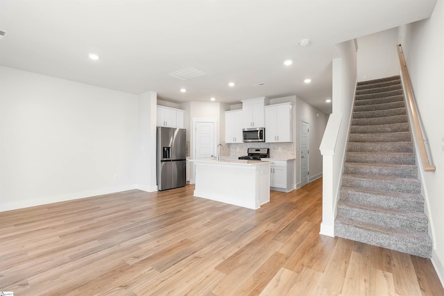 kitchen with white cabinetry, light hardwood / wood-style floors, decorative backsplash, a center island with sink, and appliances with stainless steel finishes