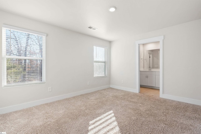 unfurnished bedroom with sink, light colored carpet, connected bathroom, and multiple windows