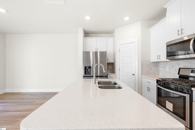 kitchen with light stone counters, stainless steel appliances, white cabinetry, and sink