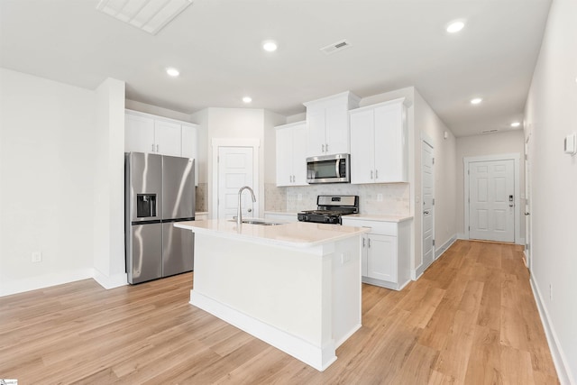 kitchen with stainless steel appliances, an island with sink, decorative backsplash, sink, and white cabinetry