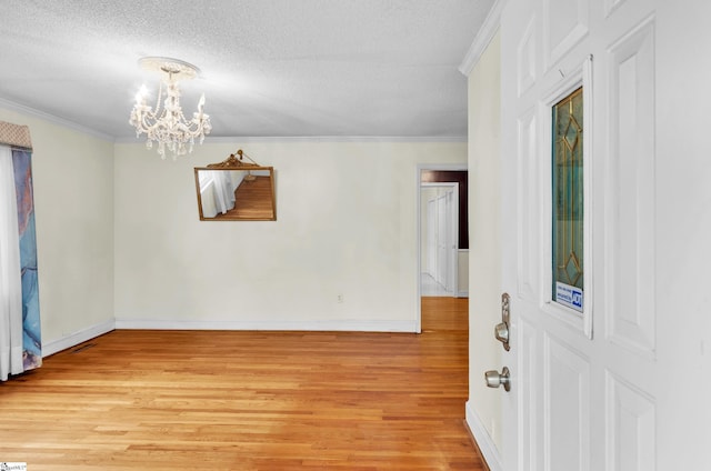 spare room featuring a textured ceiling, light wood-type flooring, an inviting chandelier, and crown molding