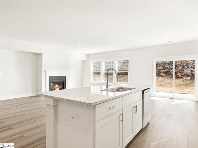 kitchen featuring sink, white cabinetry, dishwasher, light stone counters, and an island with sink