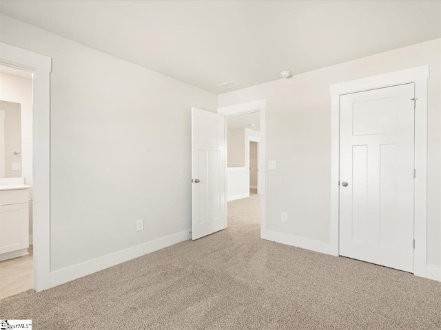 unfurnished bedroom with ensuite bath and light colored carpet