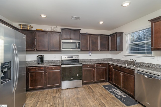 kitchen with dark stone countertops, appliances with stainless steel finishes, dark wood-type flooring, dark brown cabinetry, and sink