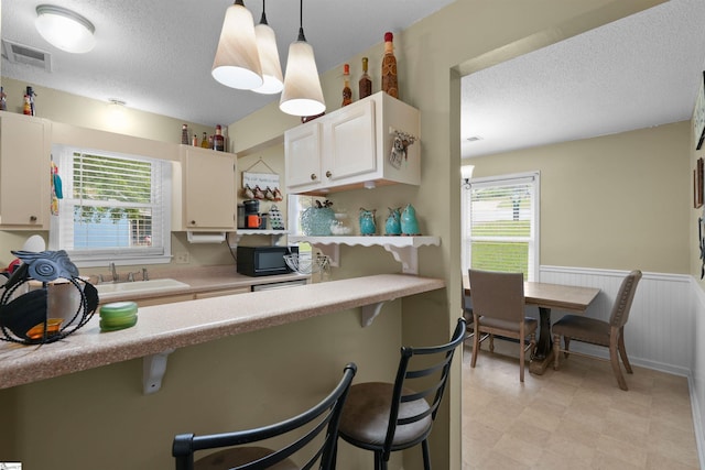 kitchen featuring sink, a breakfast bar, white cabinets, and pendant lighting