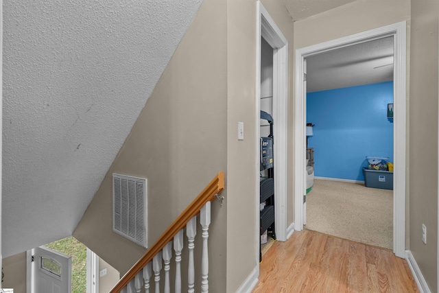 hallway with lofted ceiling, a textured ceiling, and light hardwood / wood-style flooring