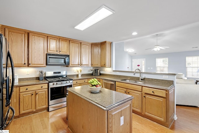 kitchen with black appliances, light wood-type flooring, ceiling fan, a kitchen island, and sink