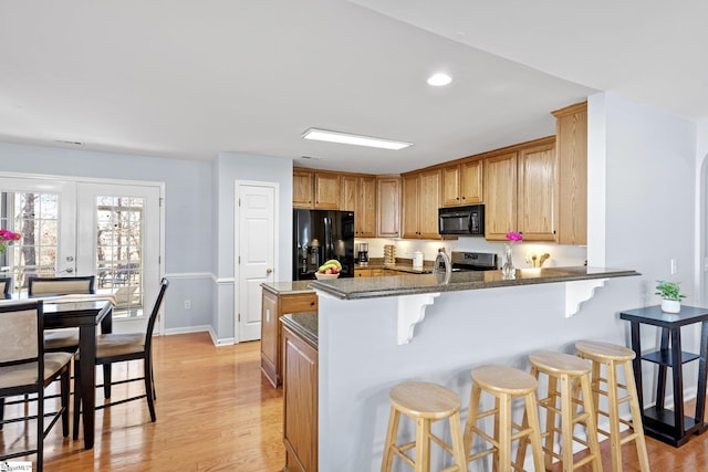 kitchen with black appliances, light hardwood / wood-style floors, kitchen peninsula, dark stone counters, and a breakfast bar