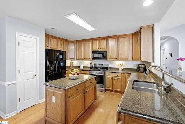 kitchen with sink, dark stone countertops, light hardwood / wood-style floors, a kitchen island, and black appliances