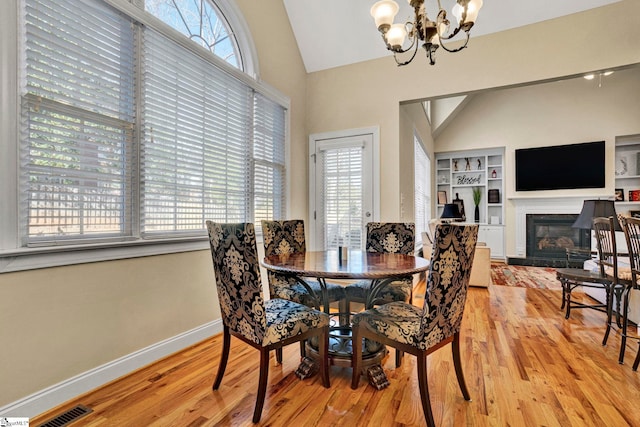 dining space with lofted ceiling, a notable chandelier, light wood-type flooring, and built in features