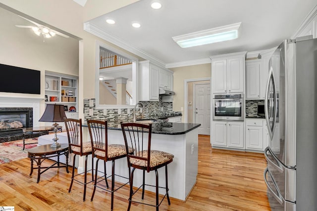 kitchen with kitchen peninsula, a high end fireplace, a breakfast bar area, white cabinets, and appliances with stainless steel finishes