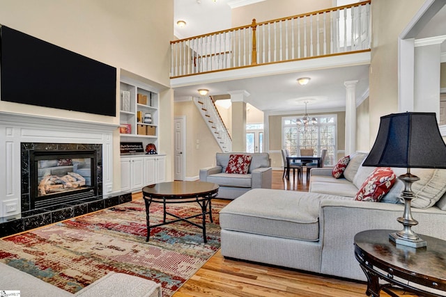 living room featuring a premium fireplace, a towering ceiling, built in shelves, light wood-type flooring, and crown molding