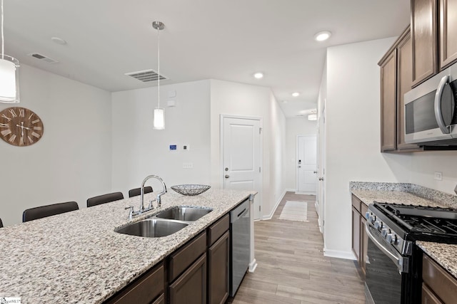 kitchen with sink, stainless steel appliances, pendant lighting, and light stone countertops