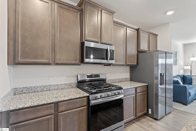 kitchen with light stone countertops, light hardwood / wood-style floors, dark brown cabinets, and appliances with stainless steel finishes