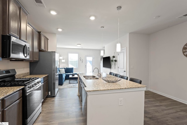 kitchen with light stone countertops, sink, a center island with sink, appliances with stainless steel finishes, and dark brown cabinetry