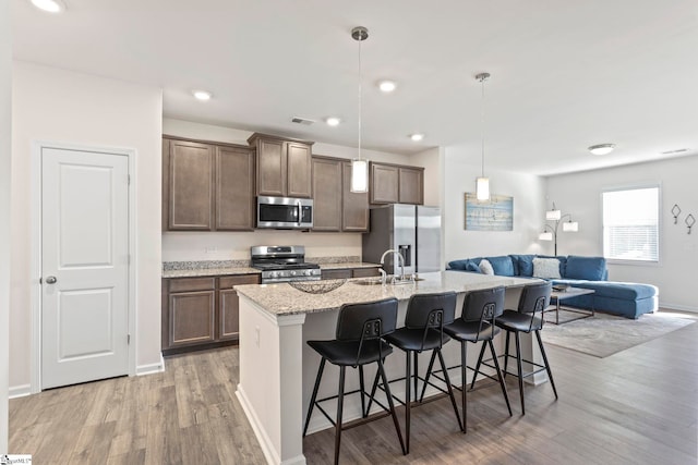 kitchen featuring appliances with stainless steel finishes, hanging light fixtures, an island with sink, a breakfast bar, and light stone counters