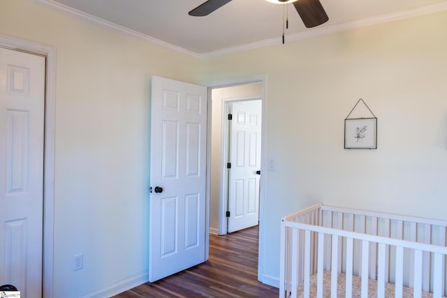 bedroom with a crib, ceiling fan, crown molding, and dark wood-type flooring