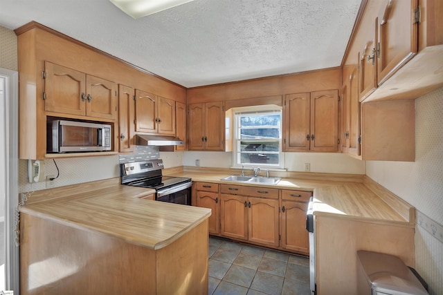 kitchen with appliances with stainless steel finishes, kitchen peninsula, light tile patterned floors, a textured ceiling, and sink