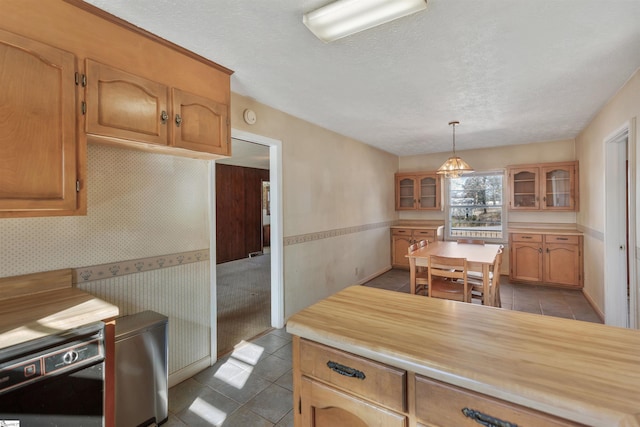 kitchen with a textured ceiling, dishwasher, pendant lighting, tile patterned flooring, and butcher block counters