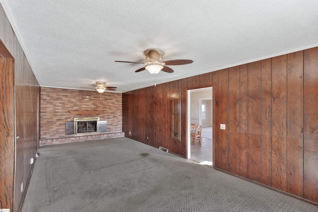 unfurnished living room featuring a brick fireplace, wood walls, ceiling fan, and light carpet