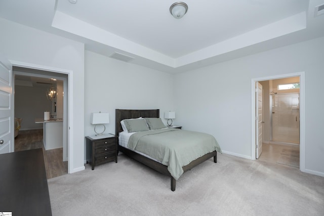 bedroom with ensuite bath, light carpet, and a tray ceiling