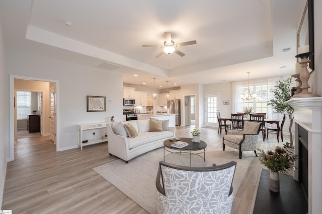 living room featuring ceiling fan with notable chandelier, light hardwood / wood-style floors, and a tray ceiling