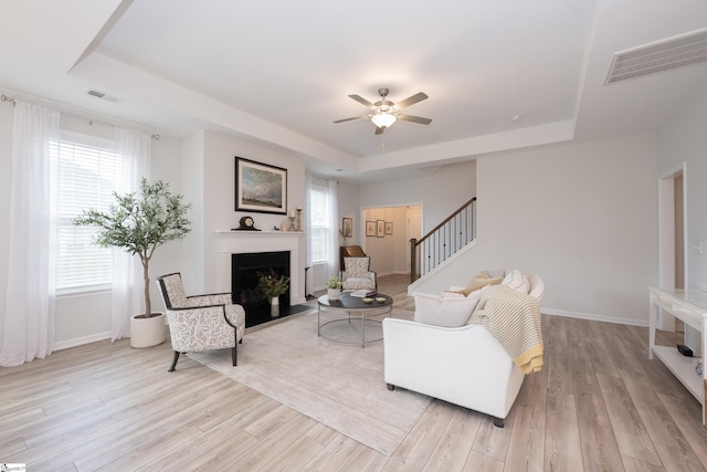 living room with a healthy amount of sunlight, a tray ceiling, and light hardwood / wood-style floors