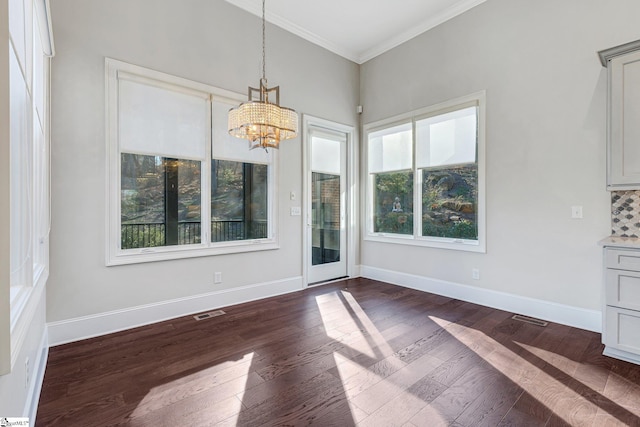 unfurnished dining area featuring a chandelier, plenty of natural light, crown molding, and dark wood-type flooring