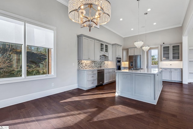 kitchen with gray cabinets, stainless steel appliances, an island with sink, decorative light fixtures, and backsplash